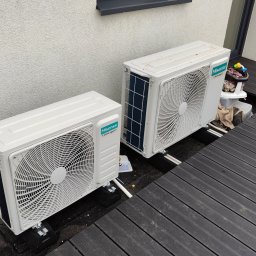MS Sanit Michał Słobodzian - Dwa białe klimatyzatory Hisense Inverter Expert zamontowane na czarnym tarasie z desek kompozytowych, z widocznymi elementami instalacji i akcesoriami dziecięcymi w tle.