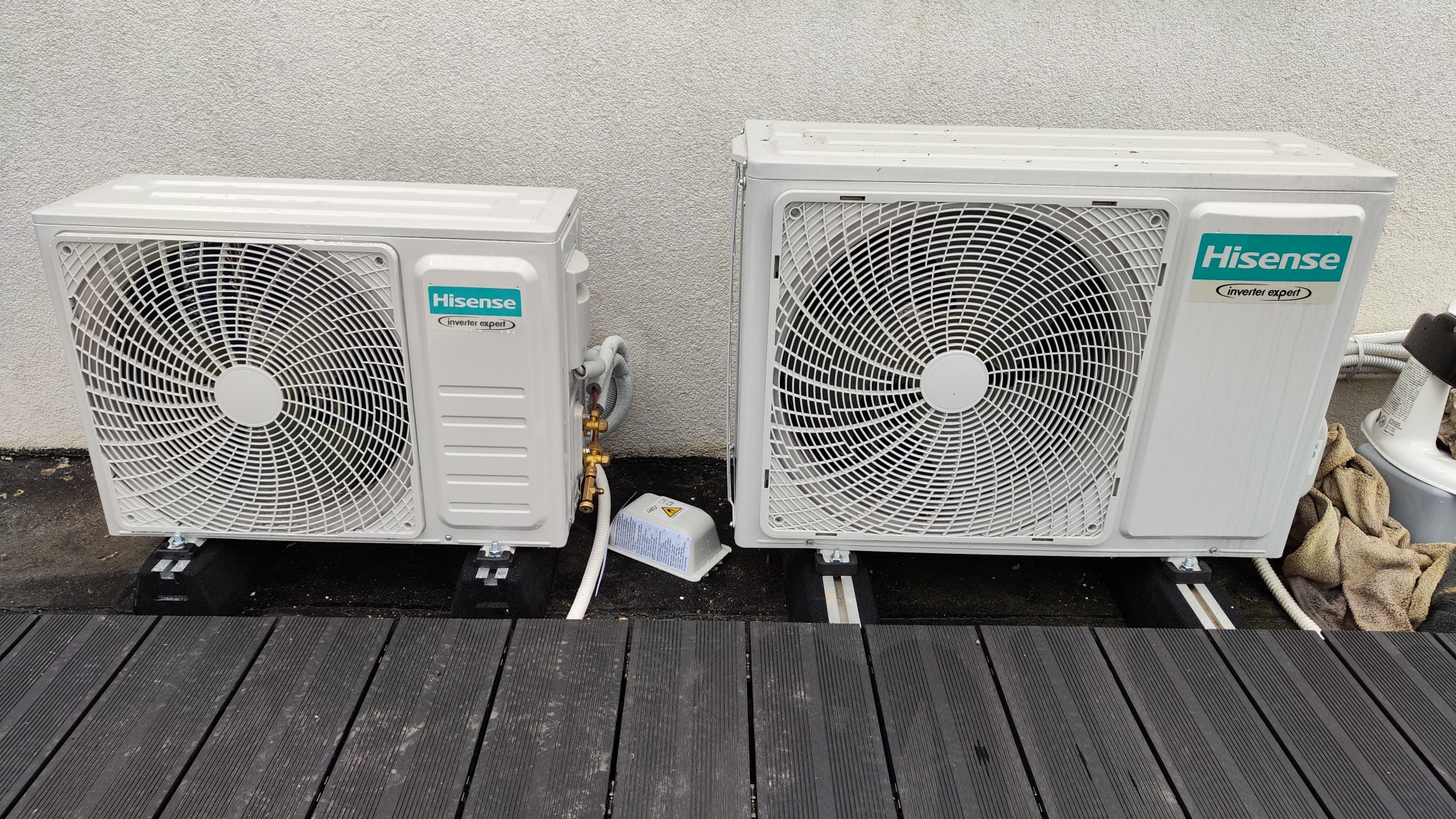 Dwa agregaty klimatyzacji Hisense zamontowane na czarnej drewnianej podłodze tarasu, widoczne miedziane rurki i elementy montażowe.