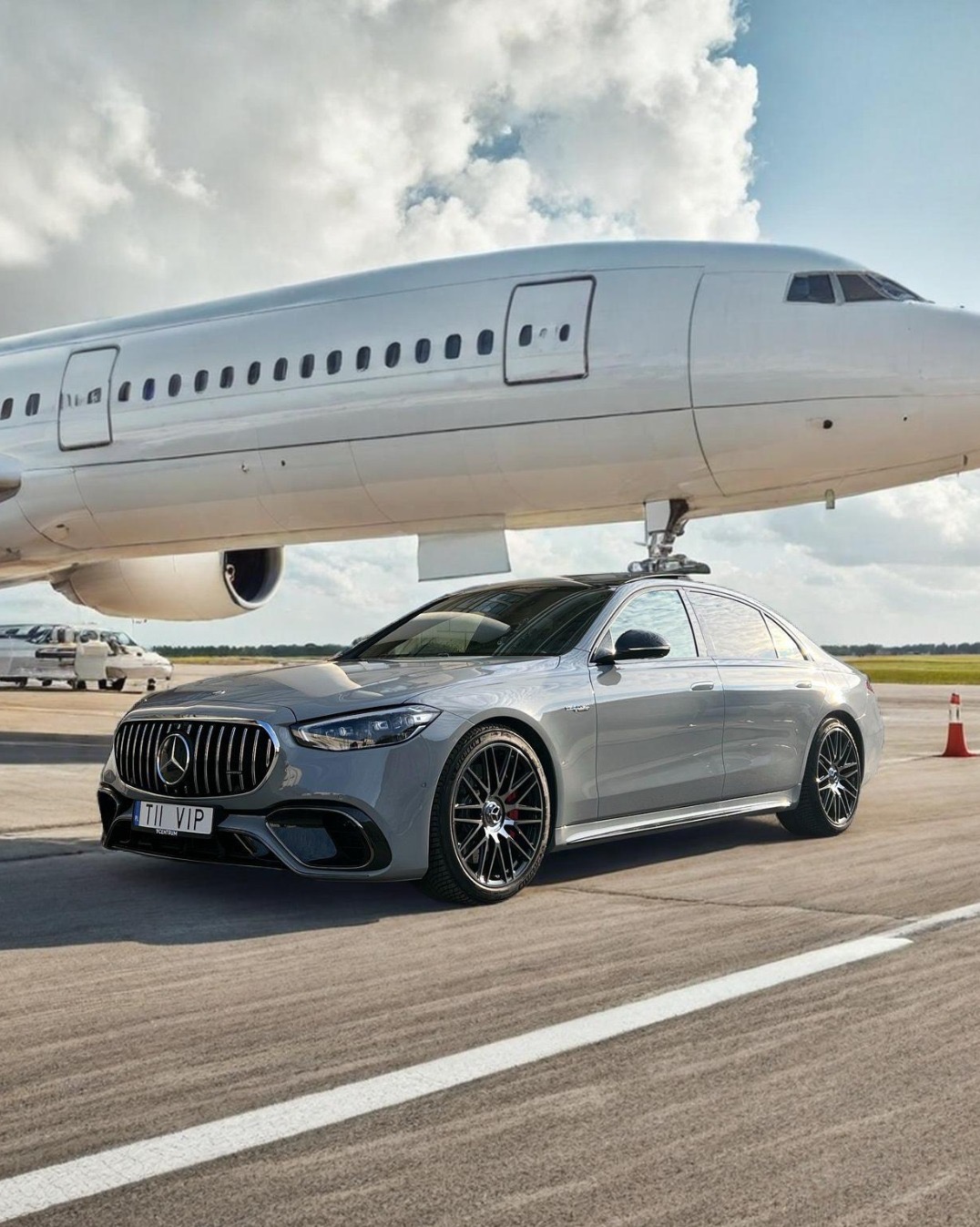 Szary Mercedes-Benz S-Class AMG zaparkowany przed białym samolotem odrzutowym na płycie lotniska w słoneczny dzień. Tablica rejestracyjna 'TII VIP'.