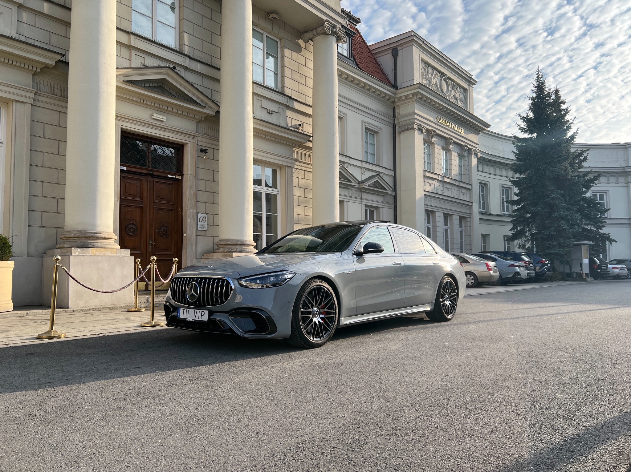 Elegancki, szary Mercedes-AMG S 63 E Performance z tablicą rejestracyjną 'TI VIP' zaparkowany przed reprezentacyjnym budynkiem z kolumnami.