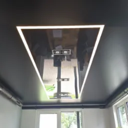 Nowoczesny, czarny sufit z trójkątnym oświetleniem LED odbijającym wnętrze biura. Widok na stół konferencyjny i okna.