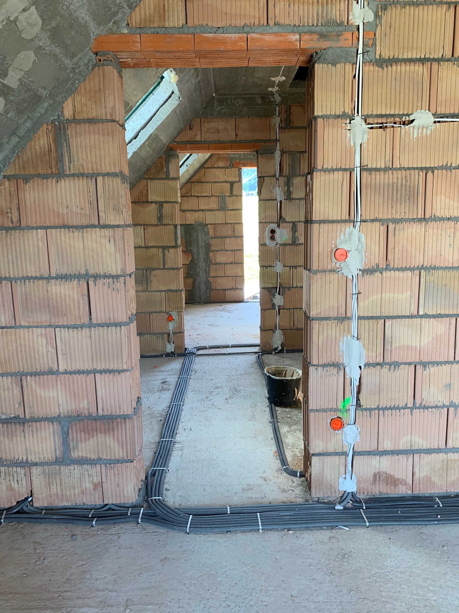 Wnętrze domu w trakcie budowy, widoczne ceglane ściany z poprowadzonymi przewodami elektrycznymi, puszki instalacyjne zamocowane na ścianach, rury karbowane ułożone przy podłodze i przymocowane...