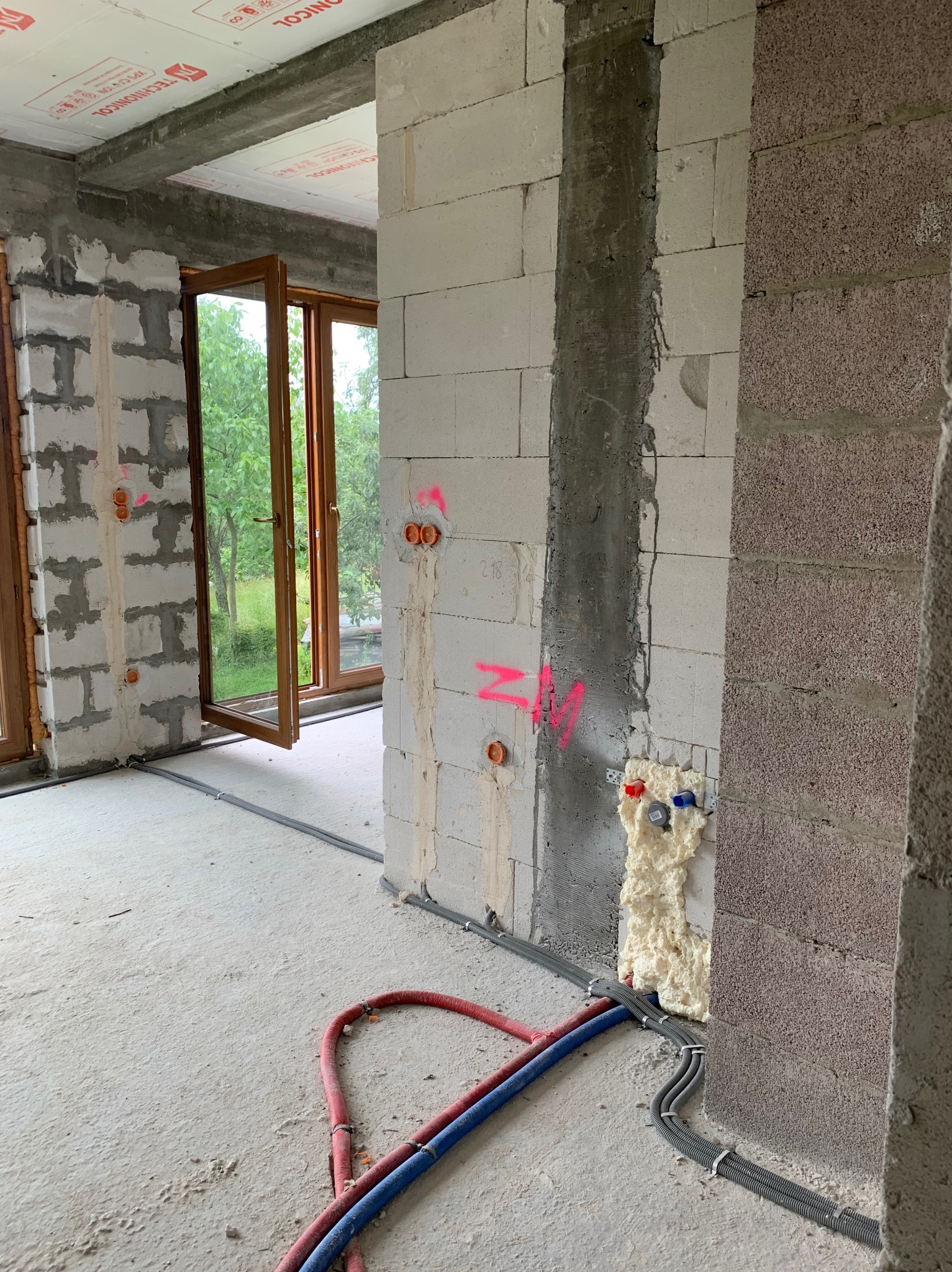 Wnętrze w stanie surowym: ściany z betonu komórkowego z instalacją elektryczną w peszlach, widoczne puszki pod gniazdka oznaczone różową farbą, rury instalacji wodnej zabezpieczone pianką montażową...