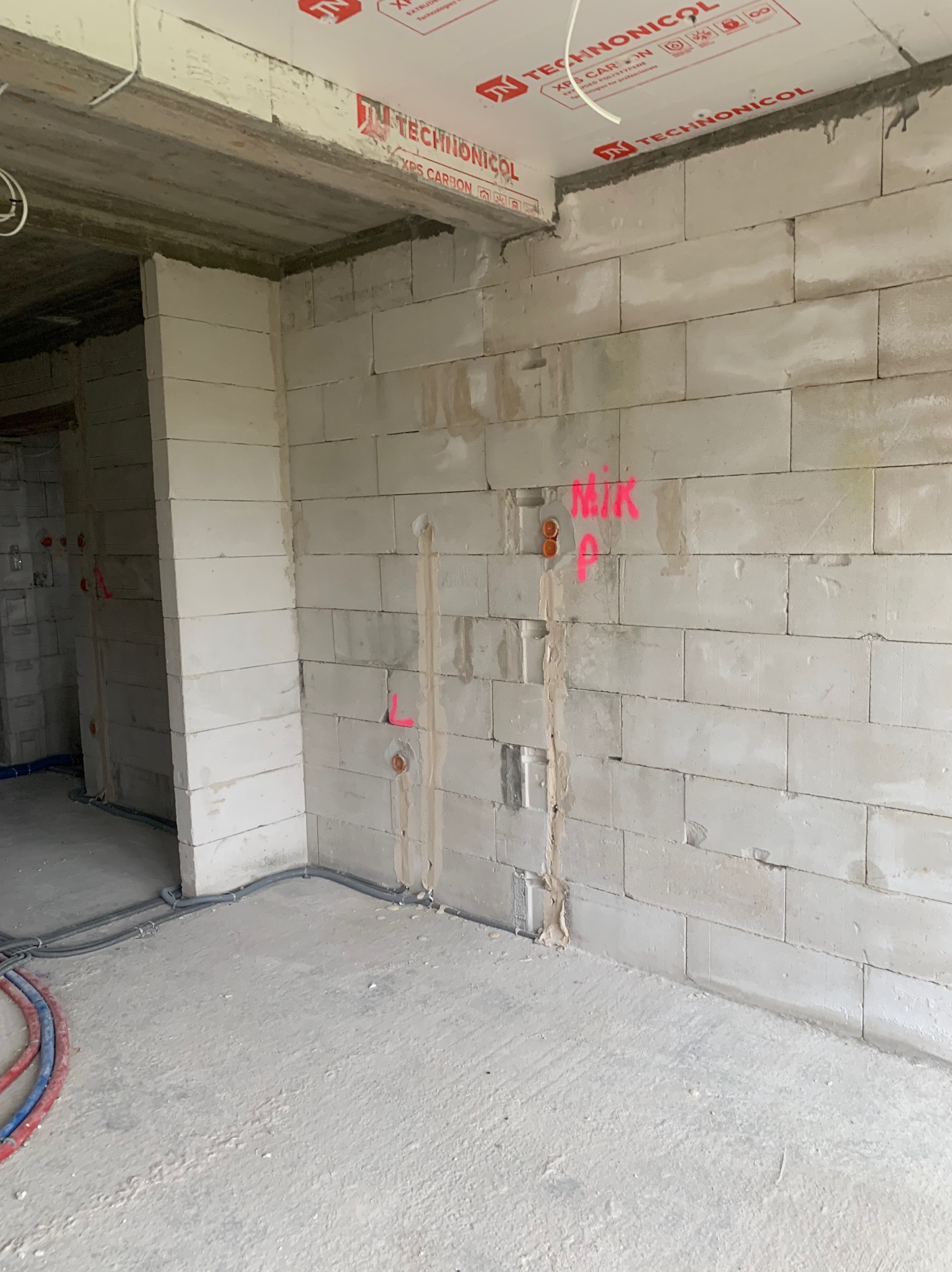 Wnętrze w stanie surowym z instalacją elektryczną w trakcie wykonywania: widoczne kable w ścianie z betonu komórkowego, oznaczenia różową farbą, strop z płyt warstwowych Technonicol.