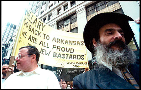 Protestujący mężczyźni trzymają transparent z napisem 'HILLARY GO BACK TO ARKANSAS WE ARE ALL PROUD JEW BASTARDS'.