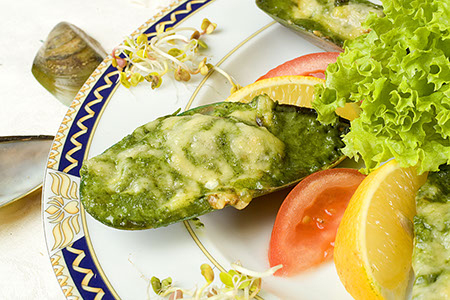 Muszle małży zapiekane z zielonym farszem i serem, podane z sałatą, pomidorem i cytryną na ozdobnym talerzu.