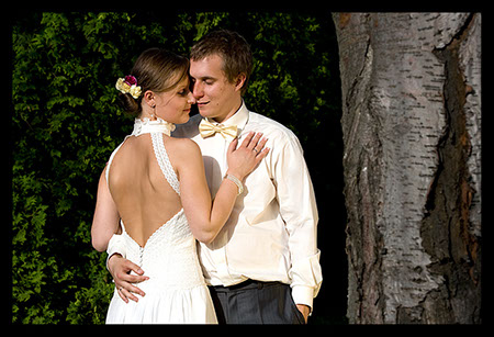 Para młoda w objęciach na tle zieleni i kory drzewa brzozy, panna młoda w białej sukni z odkrytymi plecami, pan młody w koszuli z muszką w odcieniu kremowym.