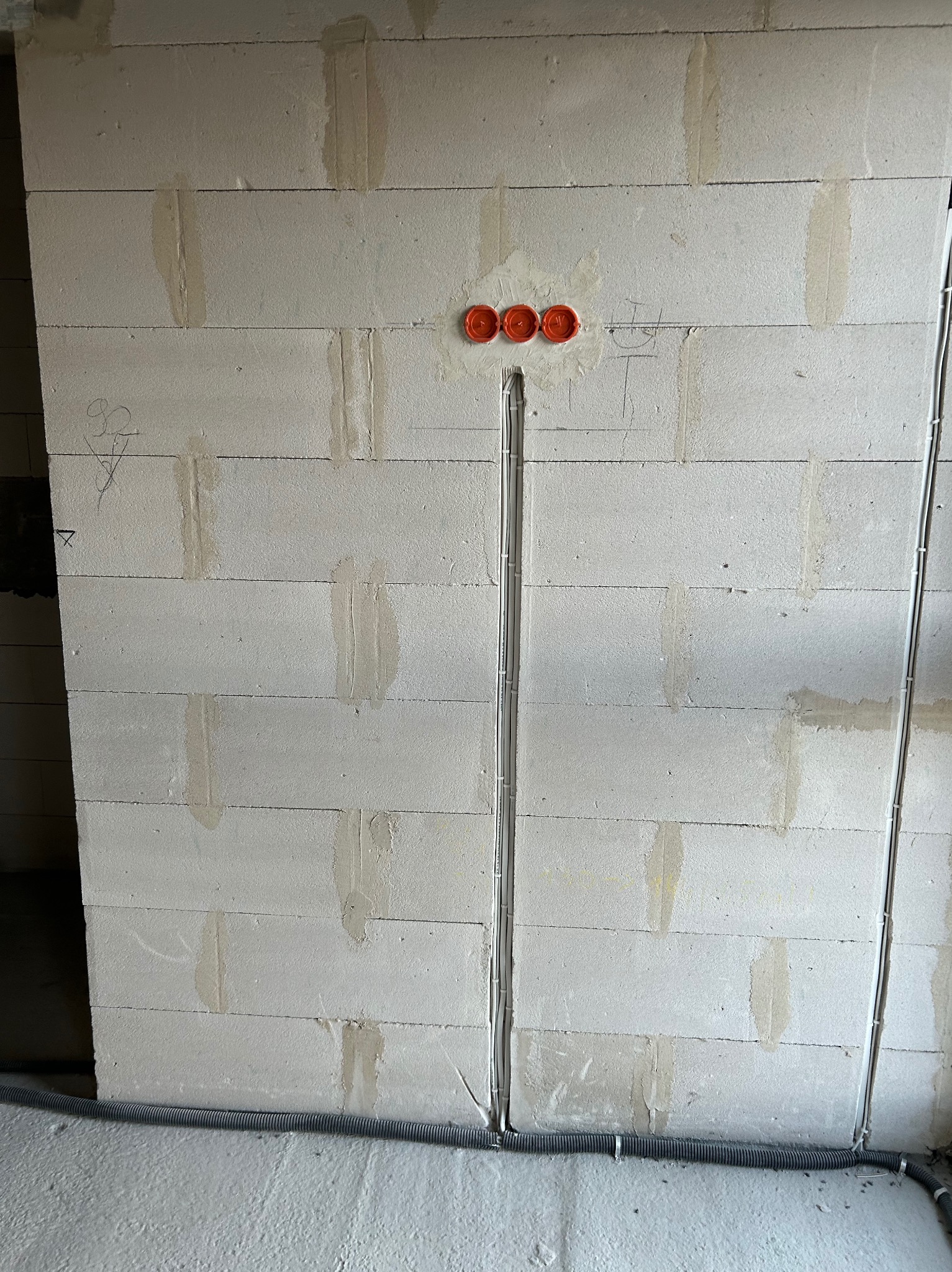 Ściana z betonu komórkowego z trzema pomarańczowymi puszkami elektrycznymi i pionowo poprowadzonymi przewodami w białych rurkach, przy podłodze rura karbowana.