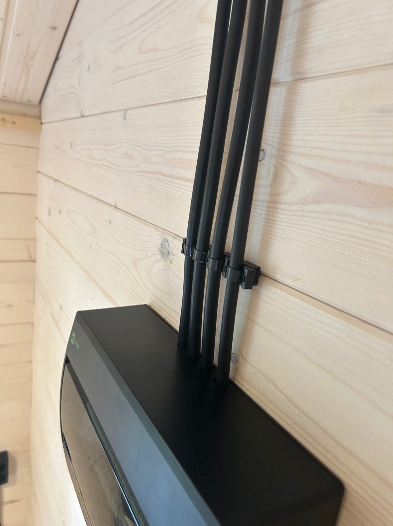 Czarna skrzynka elektryczna z czterema czarnymi kablami przymocowanymi do drewnianej ściany. Nowoczesna instalacja elektryczna wewnątrz budynku.