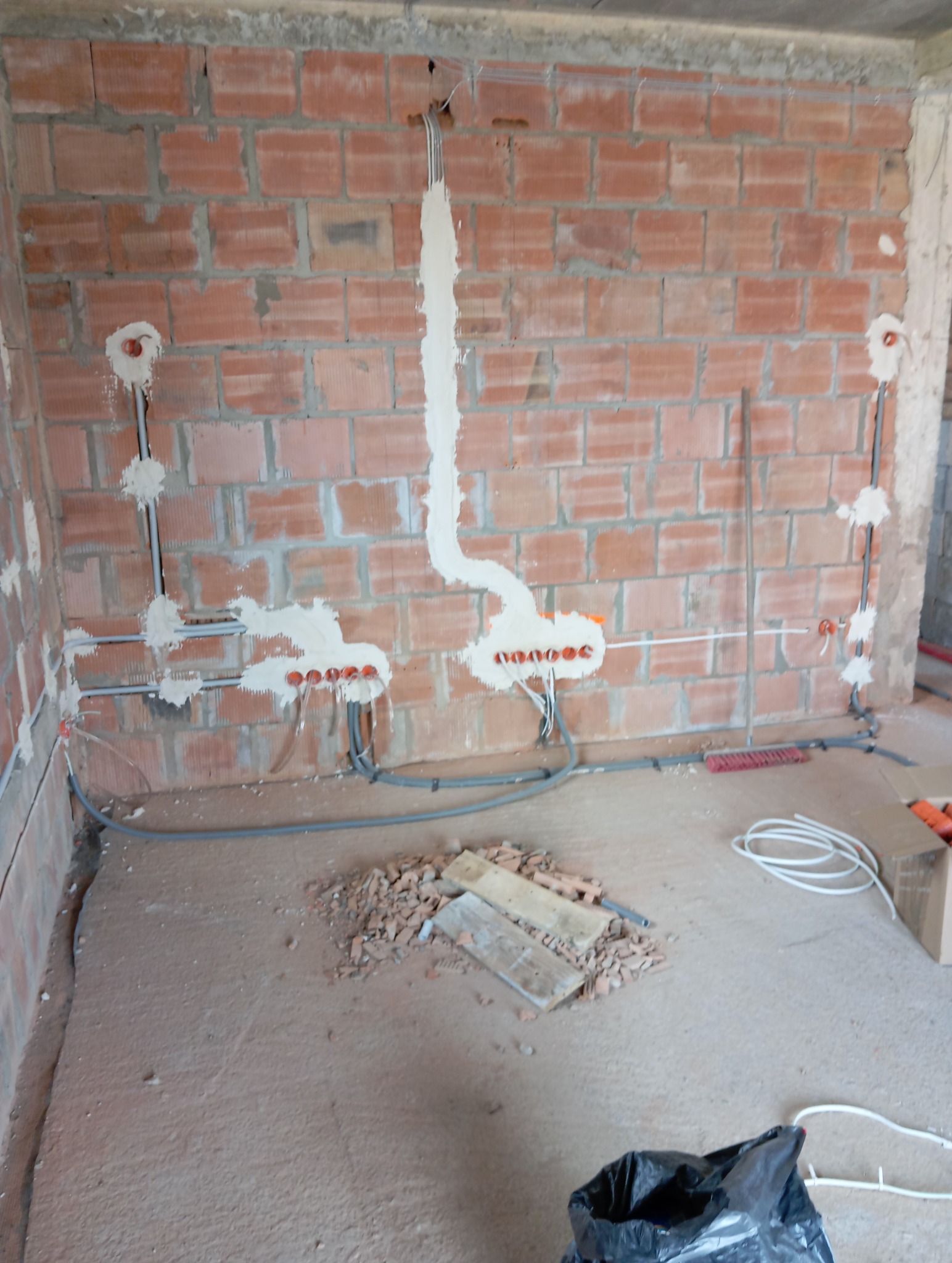 Instalacja elektryczna w trakcie montażu: przewody w ścianie z cegły, puszki elektryczne zamontowane, zabezpieczone gipsem. Etap prac instalacyjnych przed tynkowaniem.