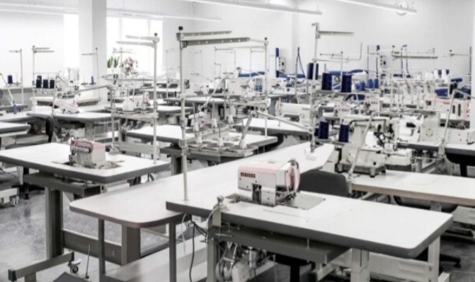 Przestronna hala produkcyjna z rzędami stanowisk do szycia, wyposażonych w maszyny i oświetlenie, z widocznymi szpulami nici w tle.