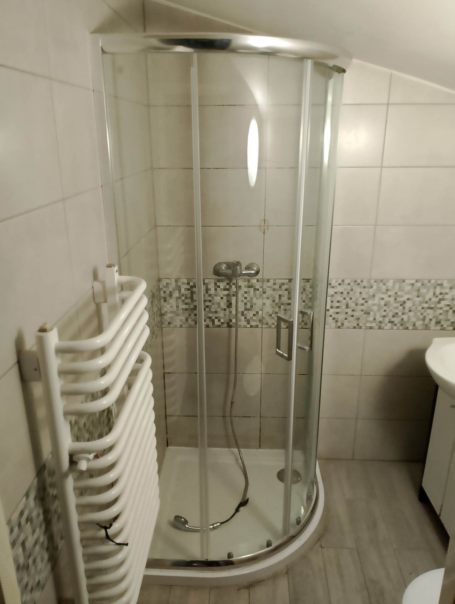 Kabina prysznicowa z grzejnikiem drabinkowym w łazience w Częstochowie, widoczne płytki ceramiczne na ścianach i podłodze.