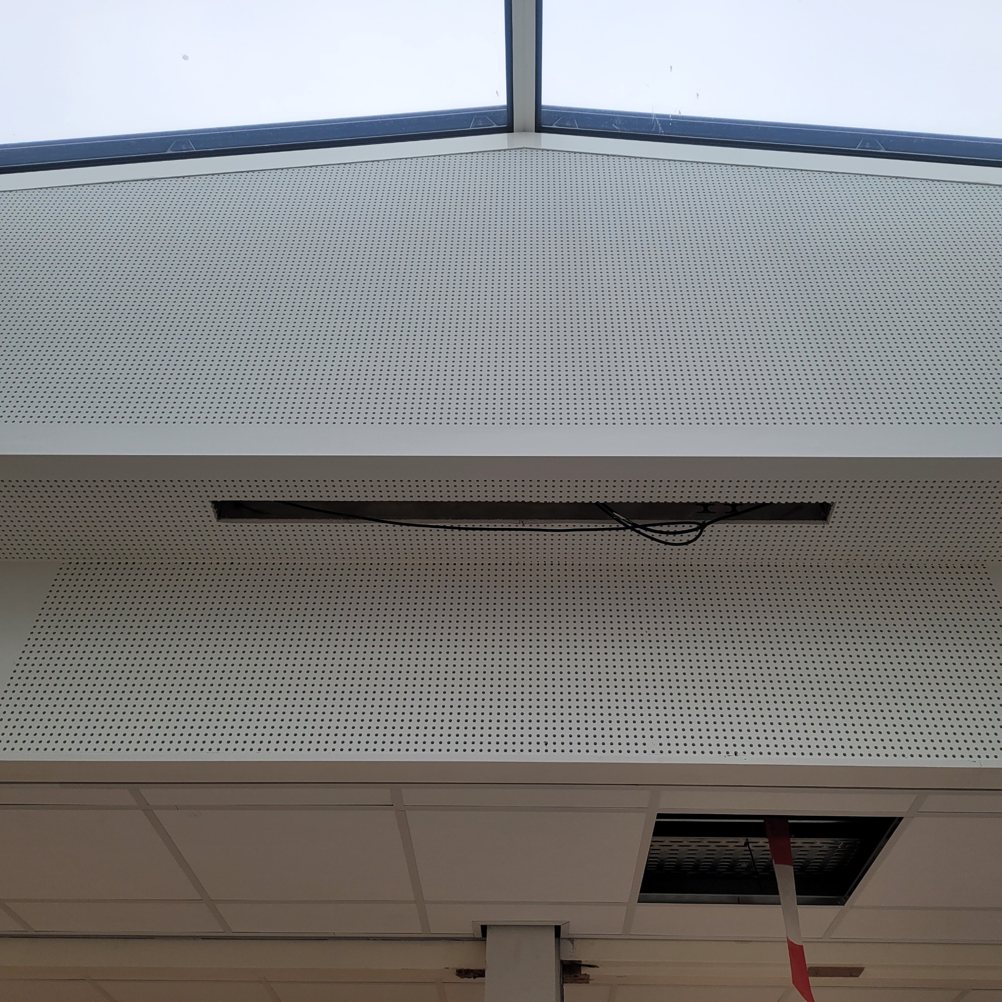 Perforowana płyta sufitowa z widocznym oknem dachowym i otwartym panelem dostępowym, ujawniającym instalację elektryczną w przestrzeni sufitowej.