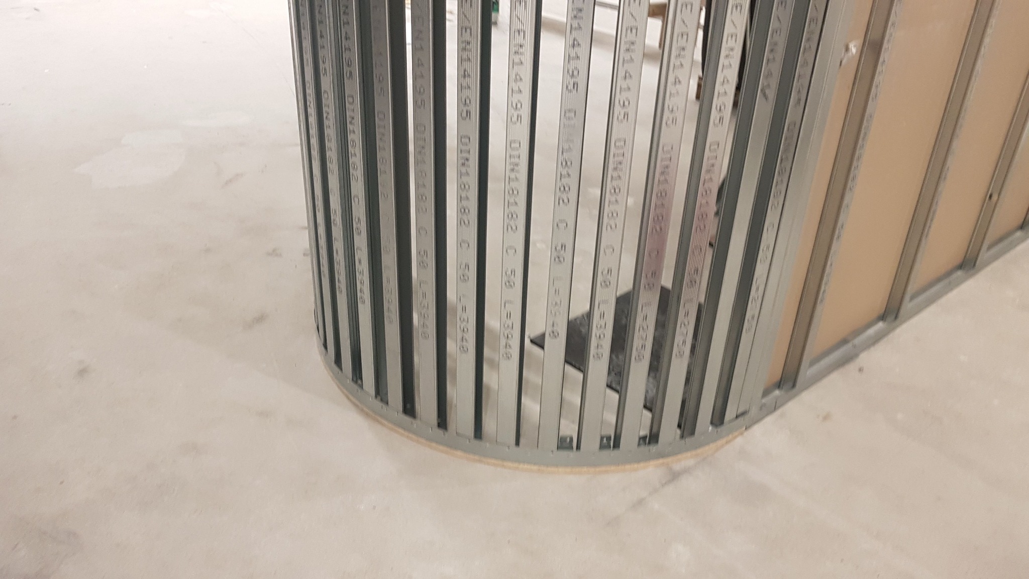 Konstrukcja z profili stalowych do montażu ścianki działowej z płyt gipsowo-kartonowych, widoczna na podłodze, z detalami technicznymi widocznymi na profilach.