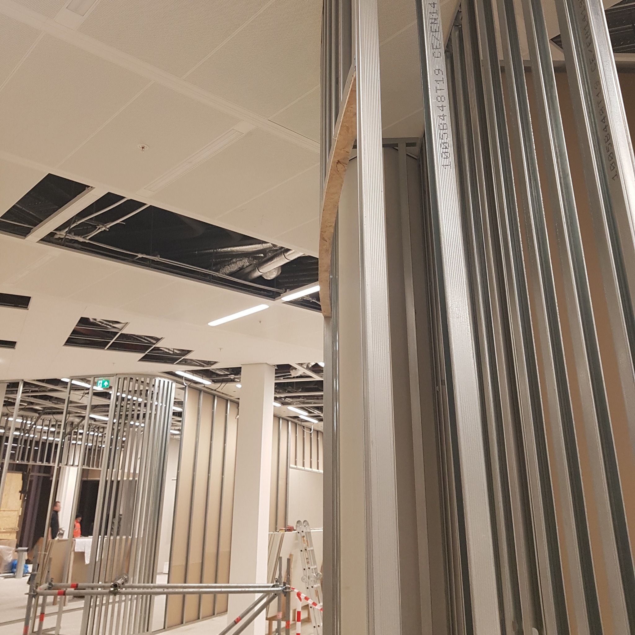 Montaż metalowej konstrukcji ścian działowych z widocznym fragmentem sufitu podwieszanego i instalacji w tle.
