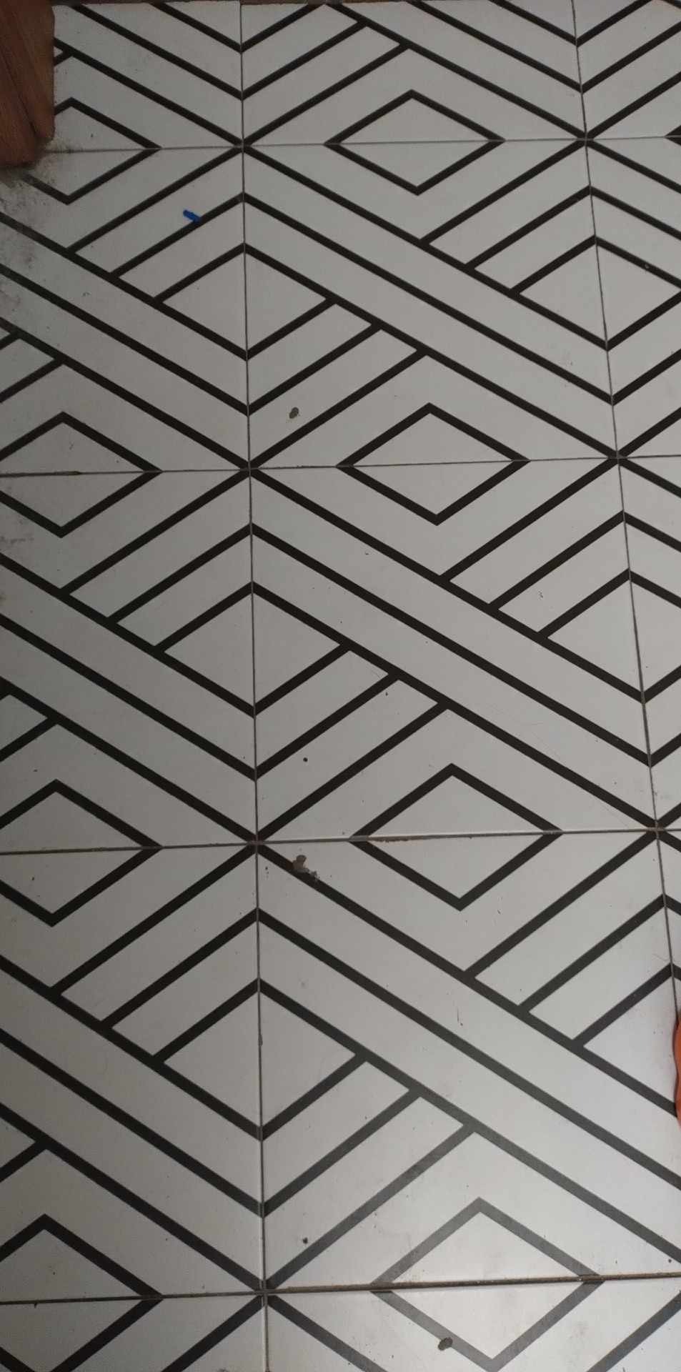 Białe płytki podłogowe z geometrycznym wzorem w czarne romby i linie, widoczne drobne zabrudzenia.
