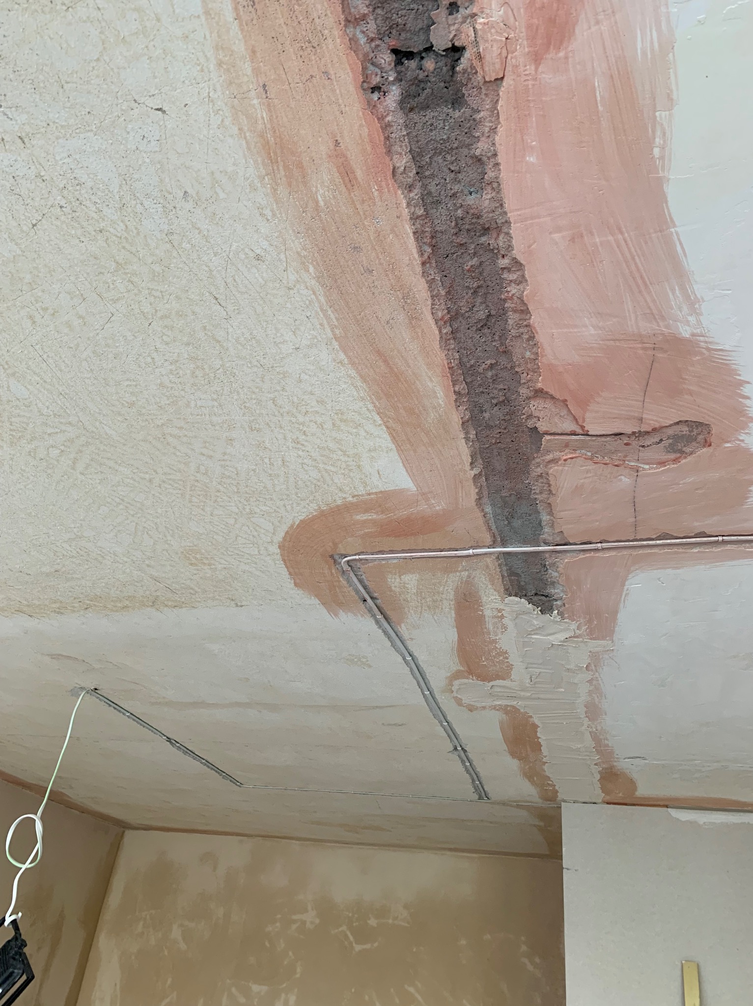 Przygotowanie sufitu do położenia instalacji elektrycznej: wyżłobione bruzdy, w których poprowadzone są kable, częściowo zamaskowane różową farbą gruntującą.