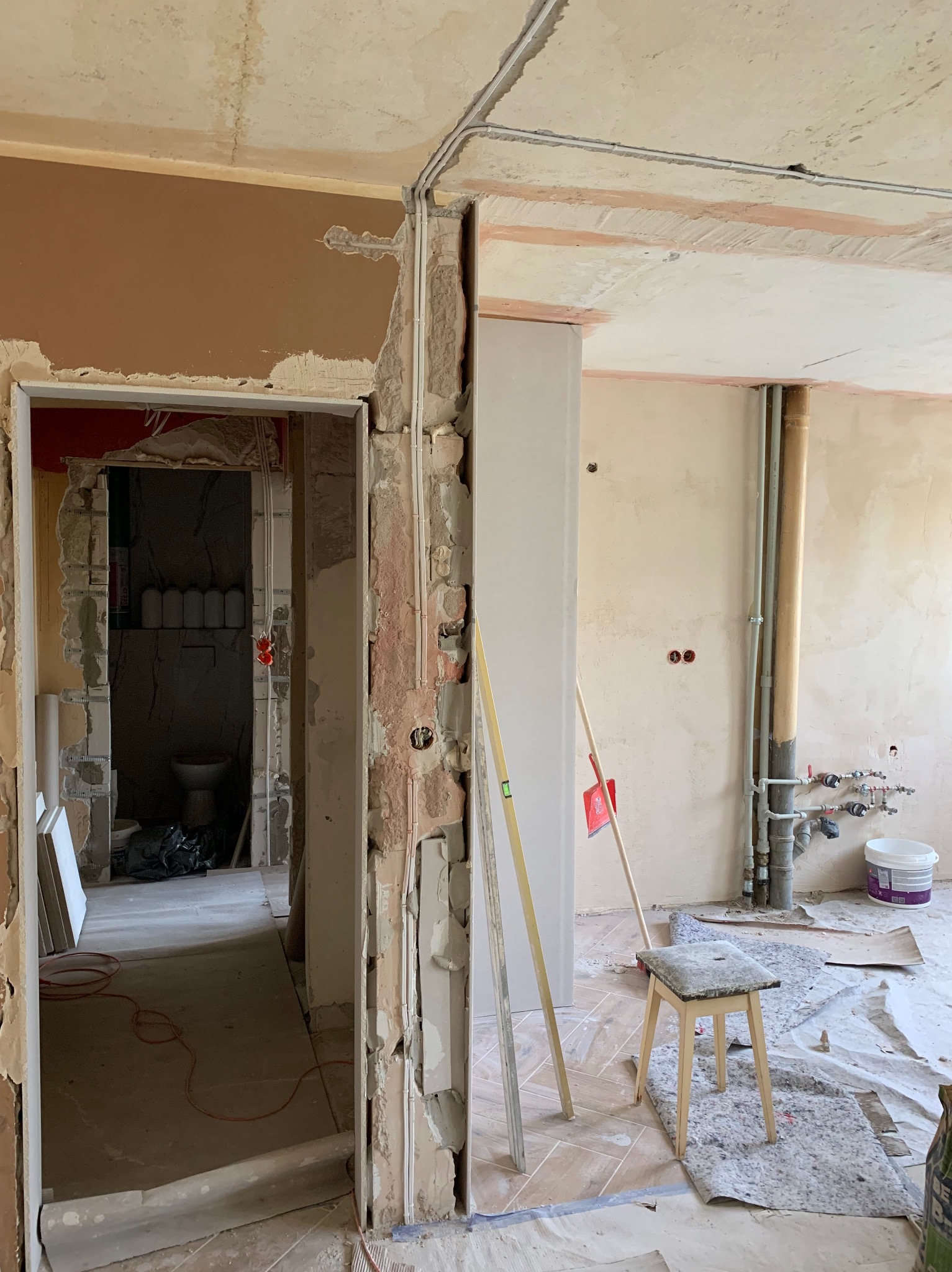 Remont mieszkania w trakcie: widoczne przewody elektryczne w ścianie, przygotowane do montażu gniazdka, fragment instalacji hydraulicznej i surowe wykończenie ścian.