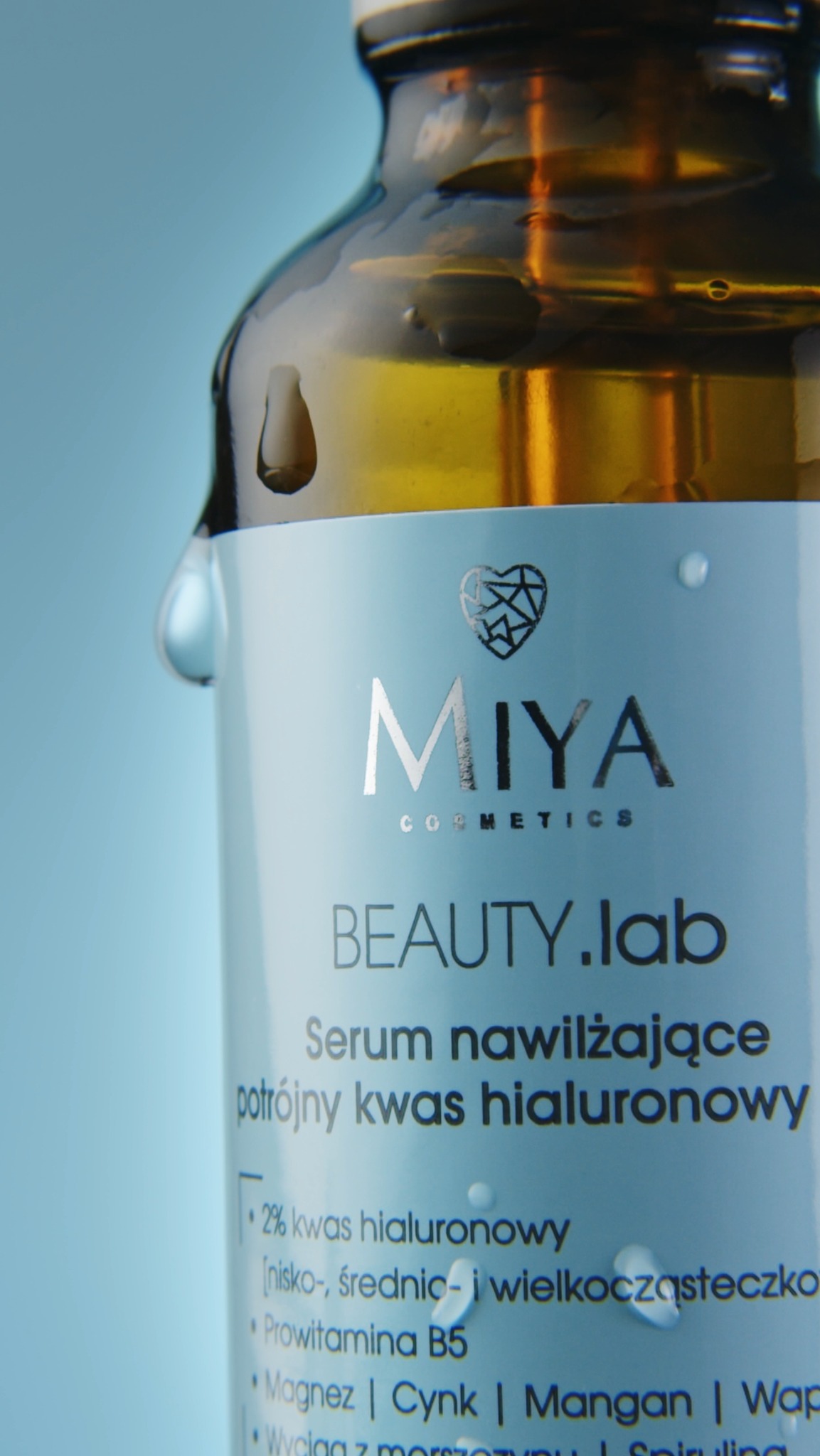 Zbliżenie na butelkę serum nawilżającego Miya Cosmetics z kroplami na etykiecie i szyjce, na jasnoniebieskim tle.