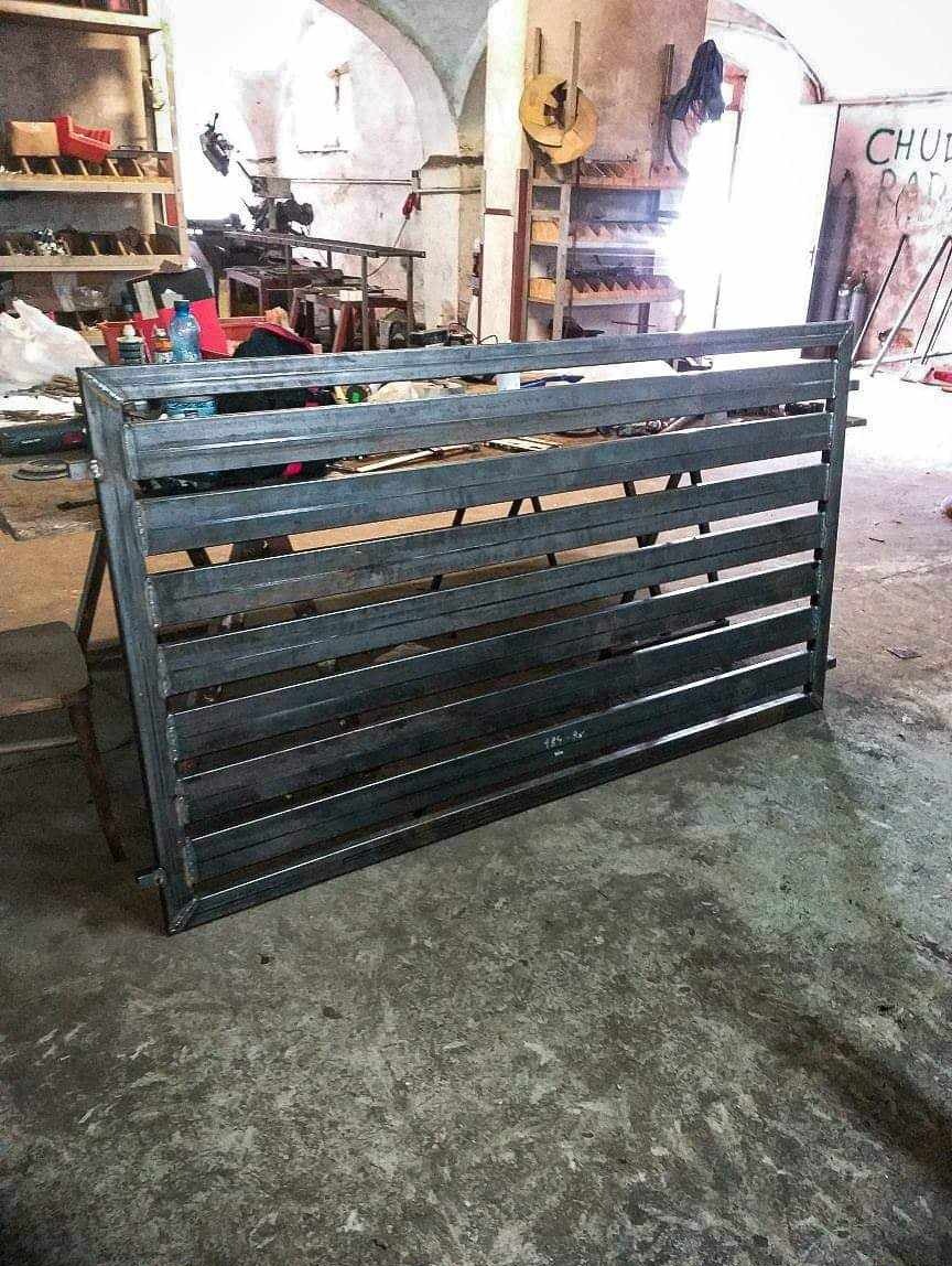 Surowy, spawany przęsło ogrodzeniowe z profili stalowych, widoczne w warsztacie, z oznaczeniami spawalniczymi, na tle regałów z narzędziami.