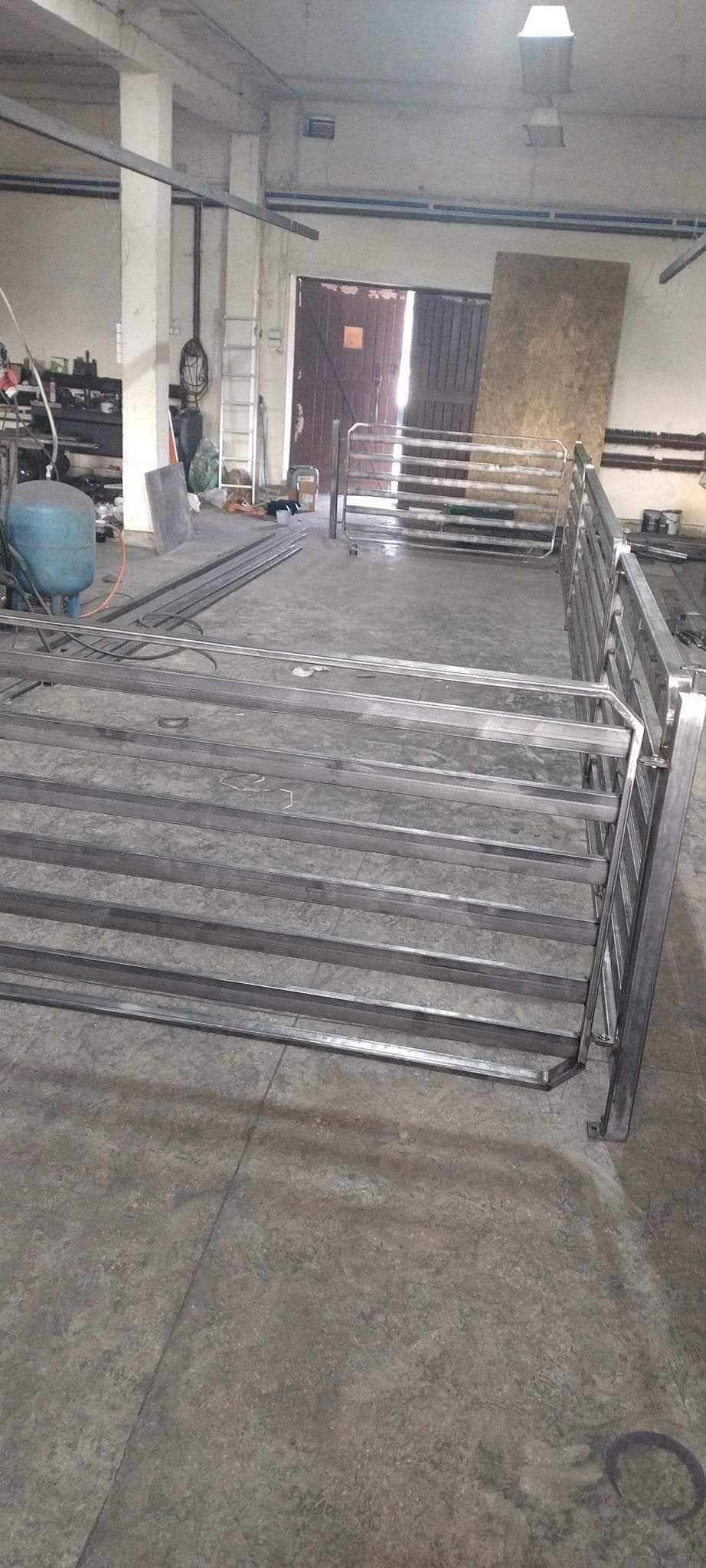 Elementy konstrukcji stalowej hali w warsztacie, widoczne profile i spawane elementy, w tle brama i drabina.