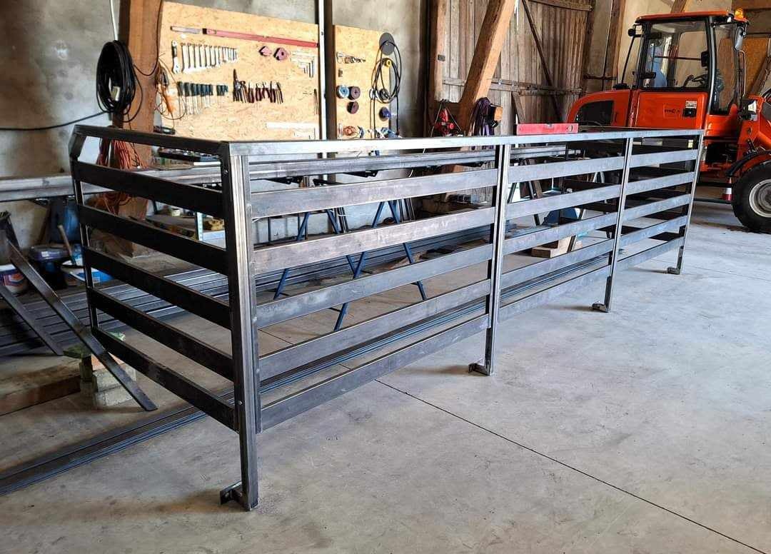 Metalowa konstrukcja hali z poziomych profili, widoczny pomarańczowy ciągnik w tle, warsztat z narzędziami na ścianie.