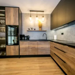 Nowoczesna kuchnia z drewnopodobnymi frontami szafek dolnych i czarnymi szafkami górnymi, oświetleniem LED pod szafkami i trzema wiszącymi lampami z żarówkami edisona, na blacie czajnik i ekspres...