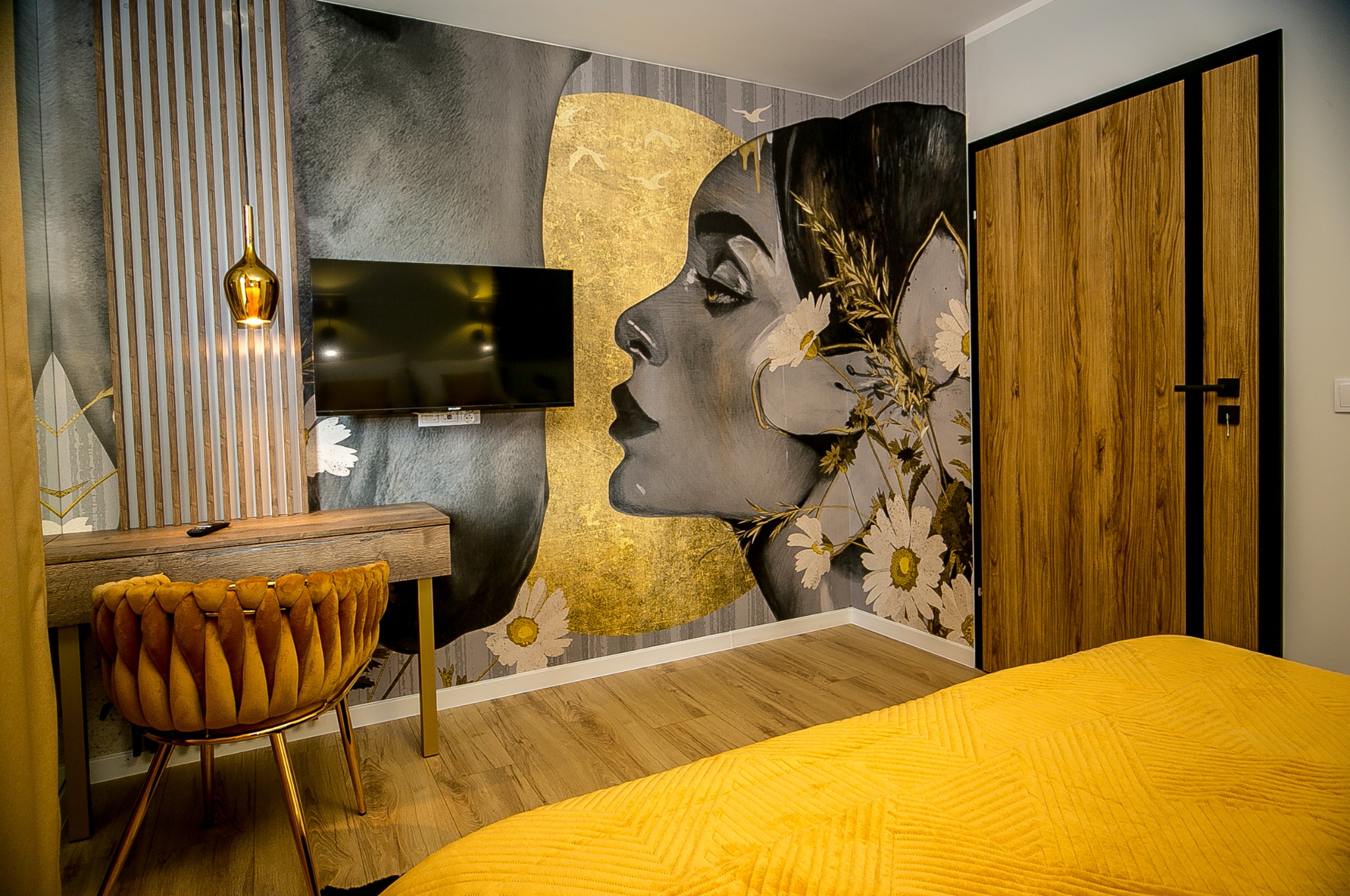 Nowoczesna sypialnia z fototapetą przedstawiającą profil kobiety z motywami kwiatowymi i złotym akcentem, biurko z krzesłem w kolorze musztardowym, drewniane drzwi z czarnymi obramowaniami i żółta...
