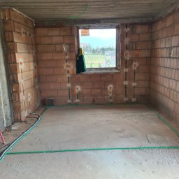 Radosław Sekuła Elektro RS - Wnętrze w stanie surowym z widoczną instalacją elektryczną w peszlach na ścianach z cegły i podłodze, przygotowane punkty pod gniazdka.