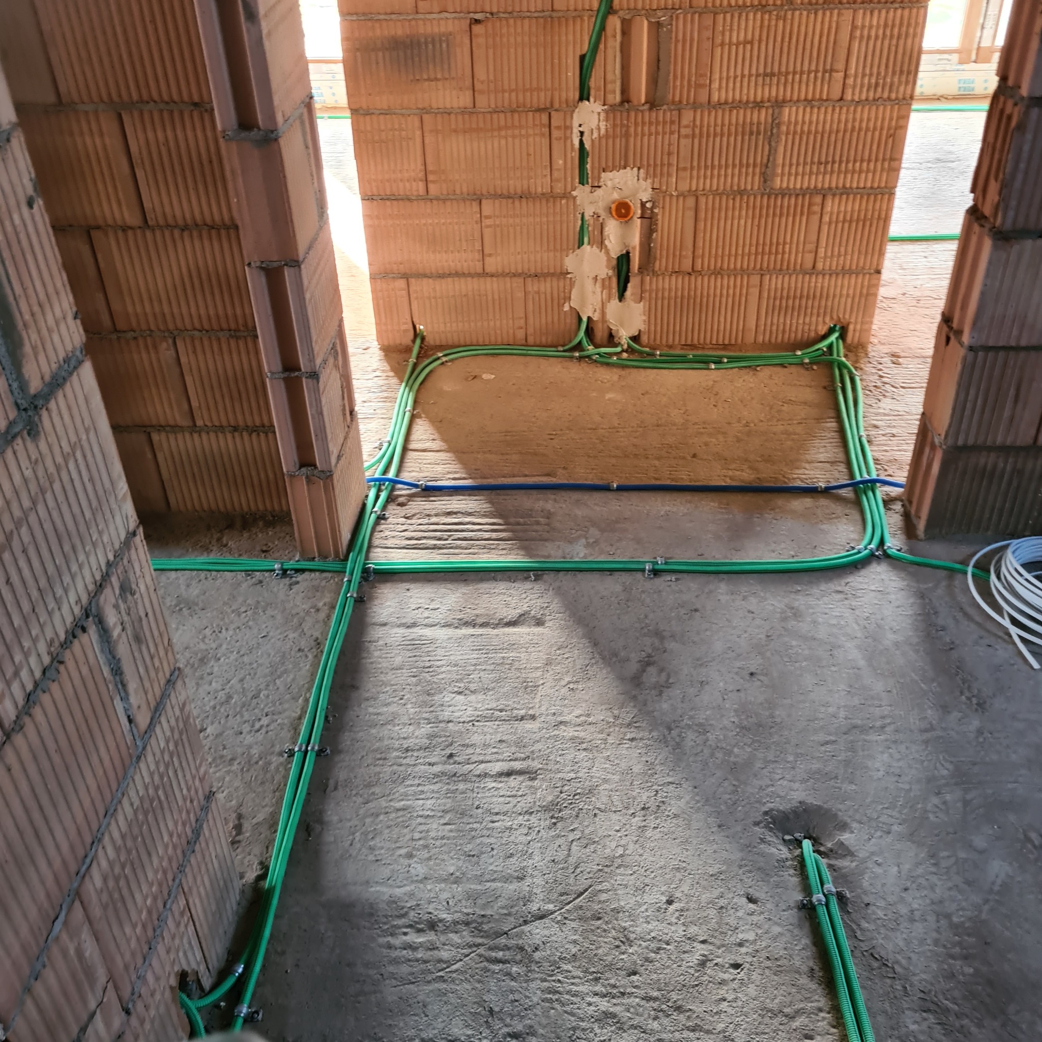 Świeżo położone, zielone rurki instalacyjne przytwierdzone do ceglanej ściany i surowego betonowego podłoża w trakcie budowy domu.