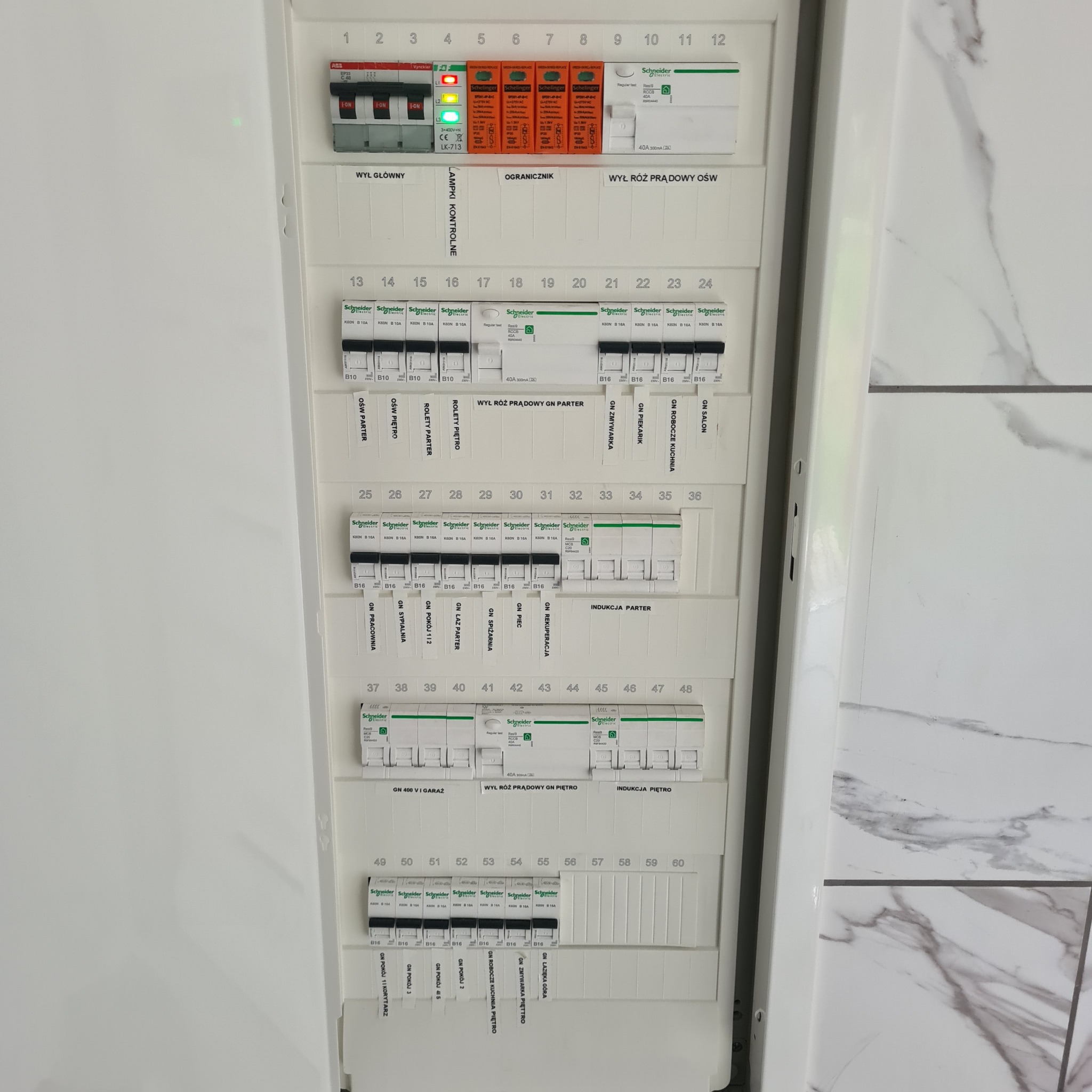 Rozdzielnica elektryczna z bezpiecznikami automatycznymi i wyłącznikami różnicowoprądowymi, opisana etykietami dla różnych obwodów w domu.