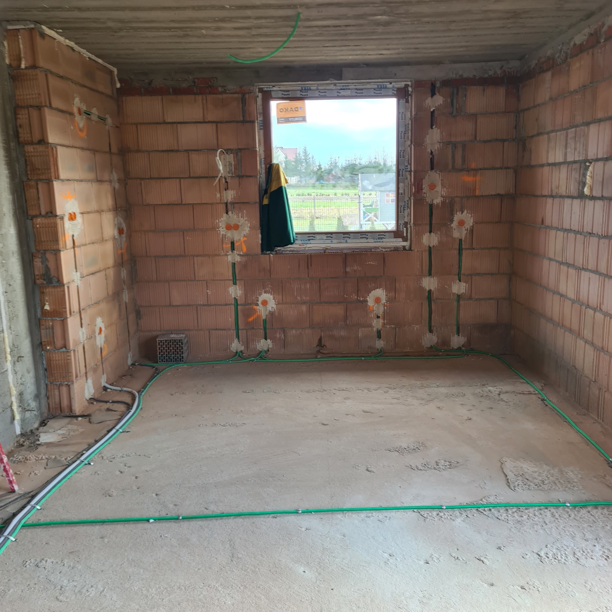 Wnętrze w stanie surowym z widoczną instalacją elektryczną w peszlach na ścianach z cegły i podłodze, przygotowane punkty pod gniazdka.