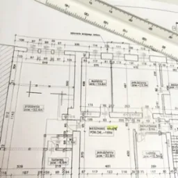 Plan mieszkania z naniesionymi wymiarami i układem pomieszczeń, częściowo zakryty przez białą linijkę. Widoczne opisy pomieszczeń i ich powierzchni.