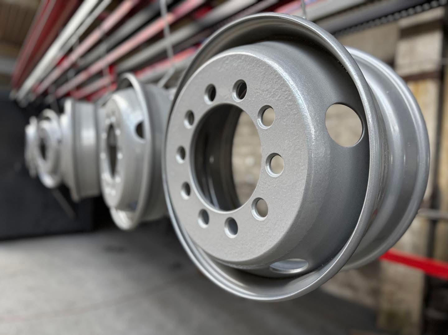 Szare, metalowe felgi samochodowe zawieszone na lince, po procesie malowania proszkowego. Widoczne otwory montażowe i gładka powierzchnia.