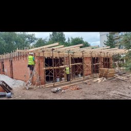 Łowas Marek - Wznoszenie ścian z czerwonej cegły na budowie w Lipnicy Wielkiej, widoczne rusztowania i pracownicy w kamizelkach odblaskowych.