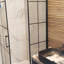 Nowoczesna kabina prysznicowa z czarnymi profilami i marmurowymi płytkami, widoczna umywalka nablatowa w kolorze grafitu, drewniana okładzina ściany, silikon sanitarny na podłodze