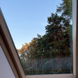 Do Ładu - Drewniane okno dachowe z widokiem na las iglasty i błękitne niebo o zmierzchu.