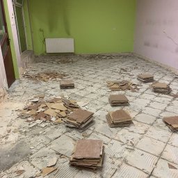 Do Ładu - Pokój w trakcie remontu, podłoga po skuciu płytek, widoczne pozostałości kleju i fragmenty płytek, ułożone w stosy nowe płytki, ściany częściowo pomalowane na zielono i różowo.