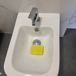 Do Ładu - Bidet marki Omnires z chromowaną baterią i żółtą gąbką w środku, na tle marmurowej ściany i ciemnej podłogi.