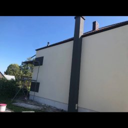 Do Ładu - Elewacja budynku po malowaniu z ciemnym kominem i obramowaniami okien, widoczne rusztowanie i pozostałości farby na ziemi.