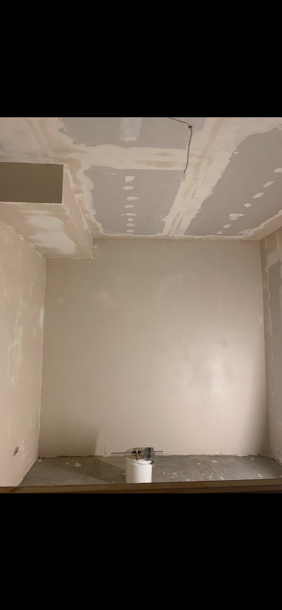 Pokój w trakcie prac wykończeniowych: ściany częściowo pokryte gładzią, widoczne ślady po szpachlowaniu na suficie i ścianach, wiadro z narzędziami na podłodze.