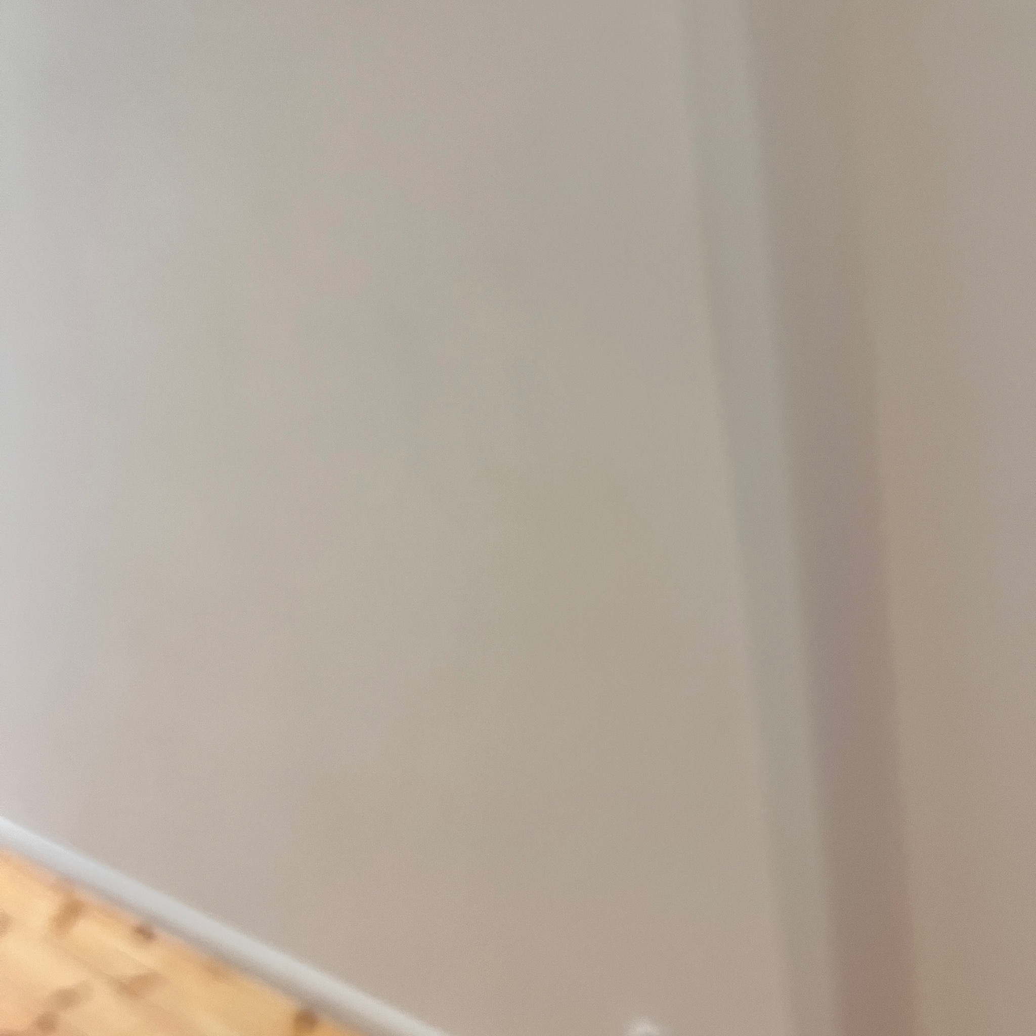 Świeżo pomalowana ściana w odcieniach beżu z widocznym fragmentem drewnianej podłogi parkietowej i listwą przypodłogową, oświetlona naturalnym światłem