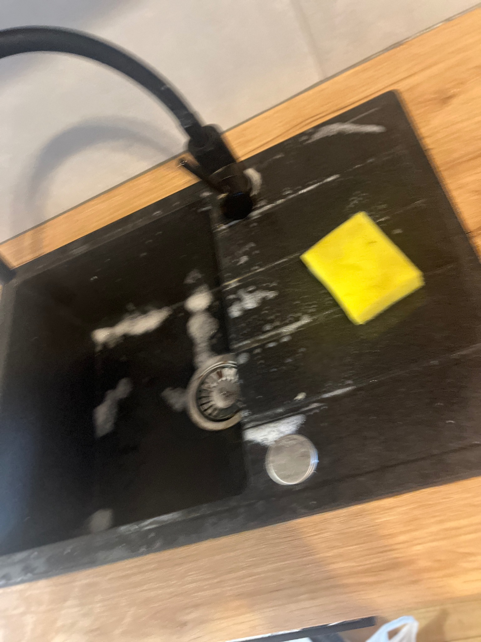 Czarny zlewozmywak granitowy z armaturą, żółtą gąbką i resztkami piany po umyciu