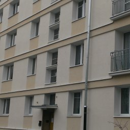 Miwobud - Odnowiona elewacja budynku wielorodzinnego z jasnobeżowymi pasami, widoczne balkony z metalowymi barierkami i rury spustowe.