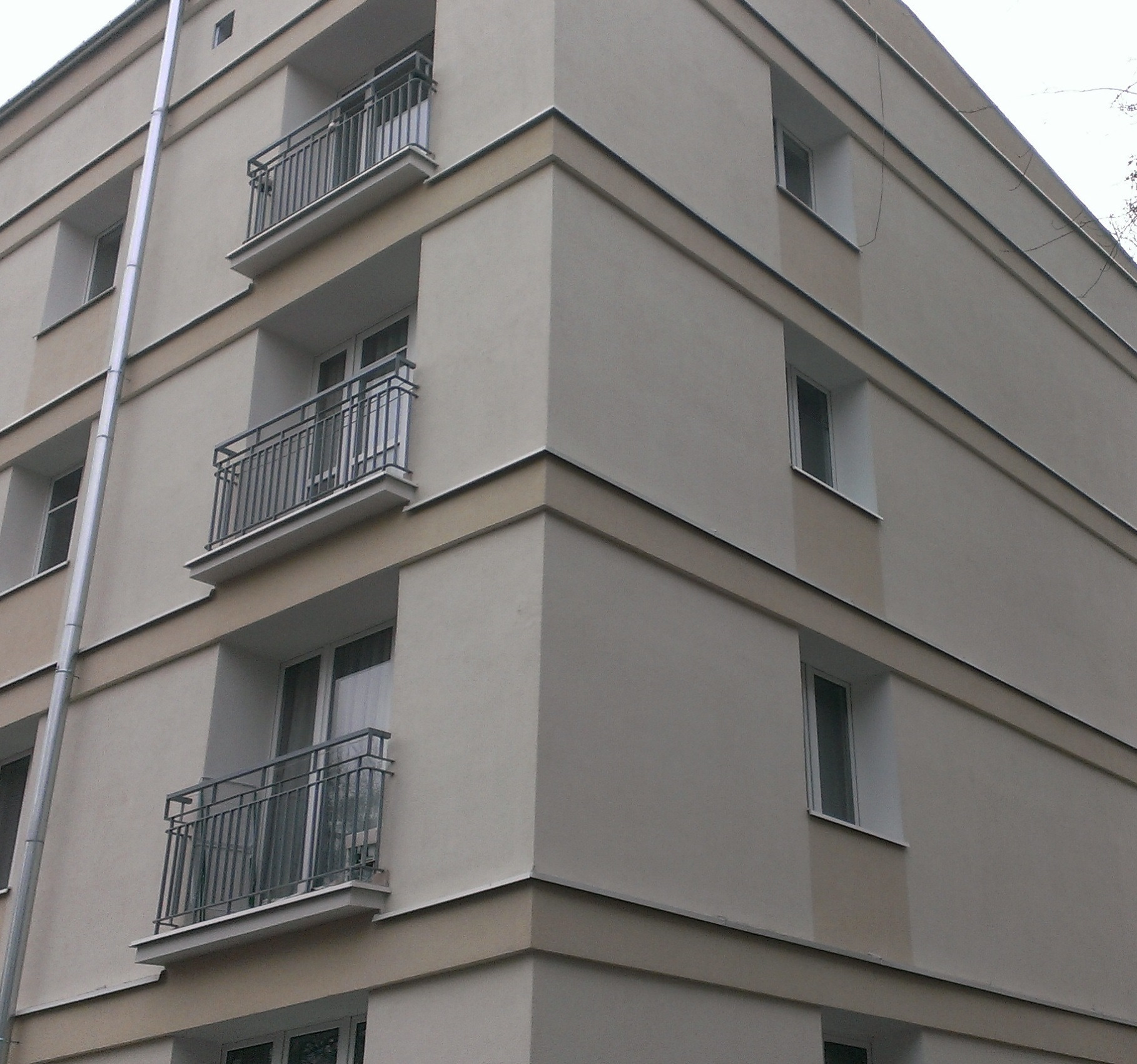 Odnowiony budynek wielorodzinny z jasną elewacją, ciemnoszarymi balustradami balkonowymi i wyraźnymi pasami w kolorze beżowym.