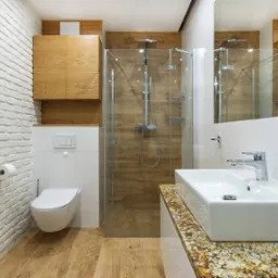 Nowoczesna łazienka z kabiną prysznicową typu walk-in, umywalką nablatową na blacie z granitu, toaletą podwieszaną i ścianą z białej cegły dekoracyjnej.