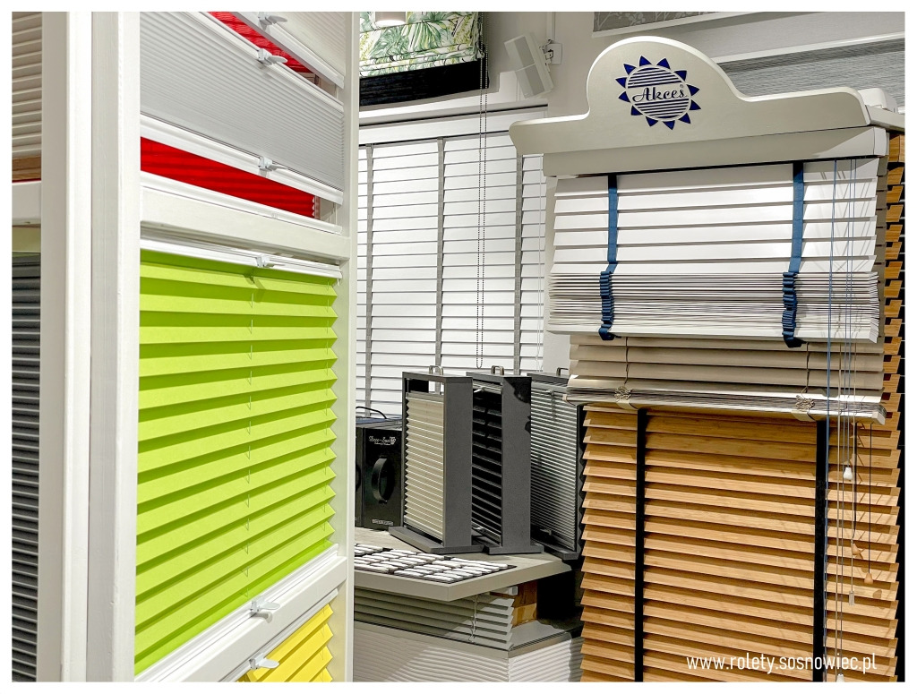 Ekspozycja różnorodnych osłon okiennych w salonie: zielone plisy, drewniane żaluzje z taśmami, oraz białe żaluzje poziome.