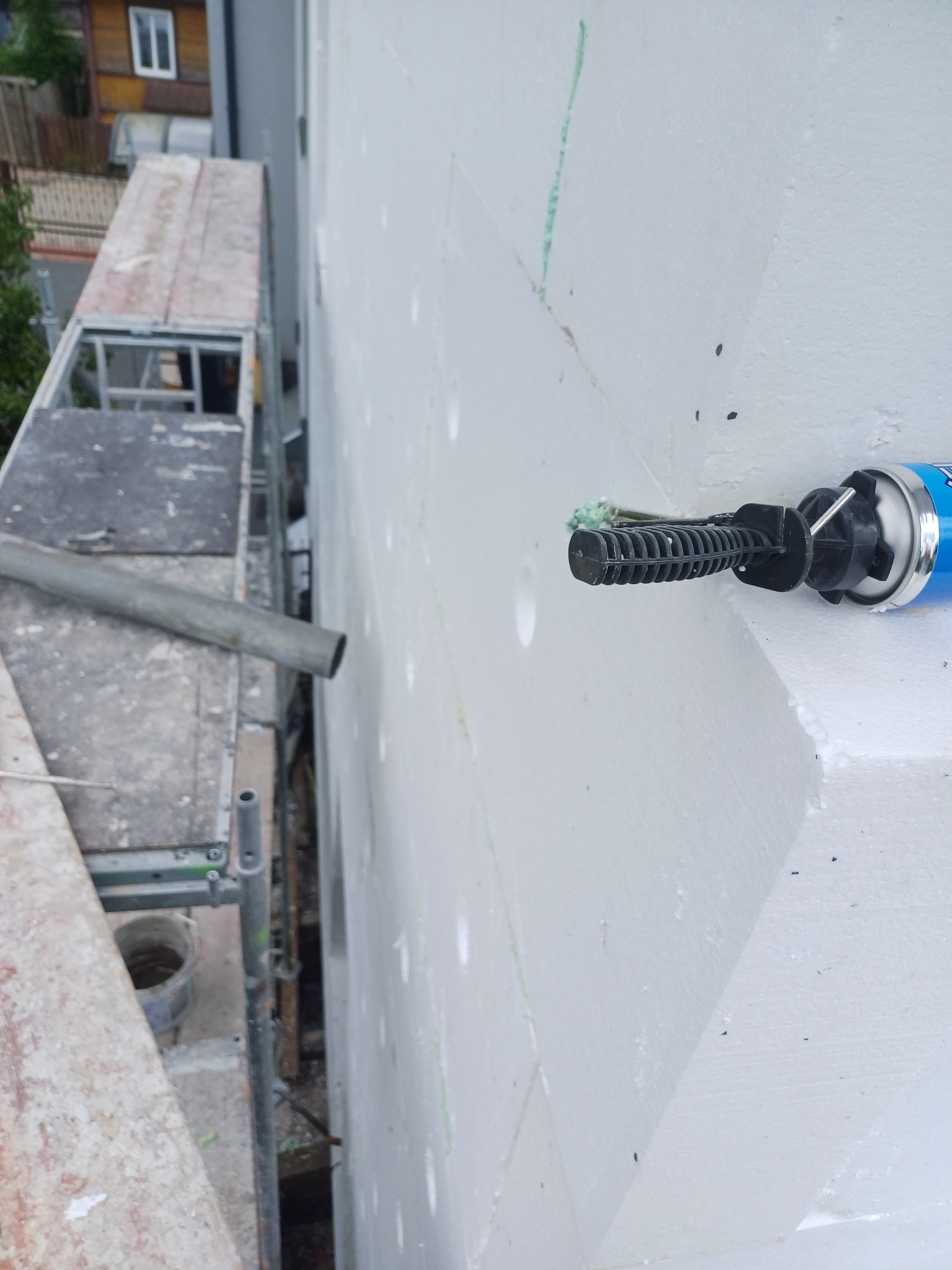 Ocieplanie elewacji budynku styropianem, widoczna puszka z pianką montażową i fragment rusztowania.