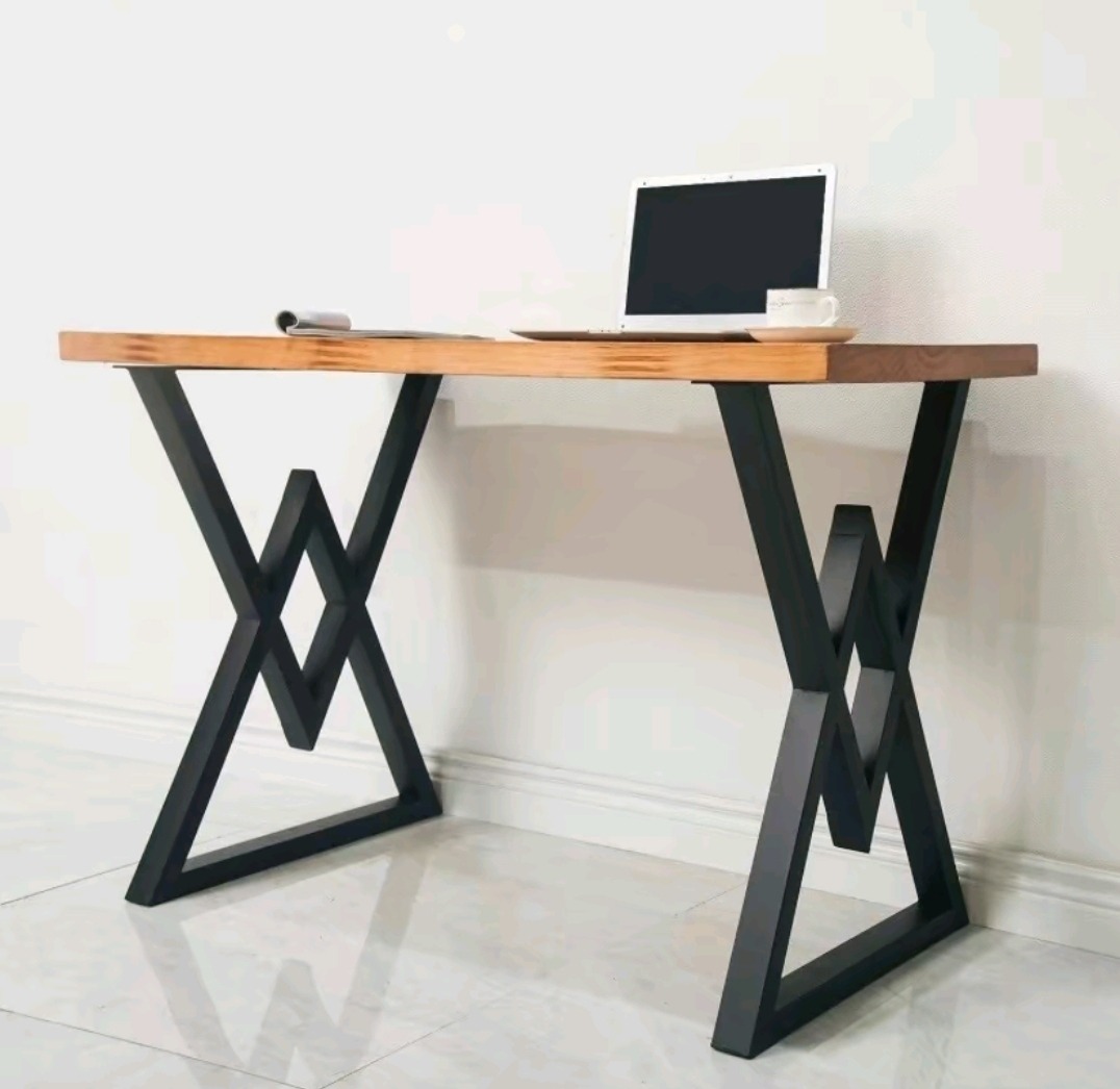 Biurko z drewnianym blatem i czarnymi, geometrycznymi nogami w kształcie połączonych trójkątów, na blacie laptop, filiżanka i gazeta.