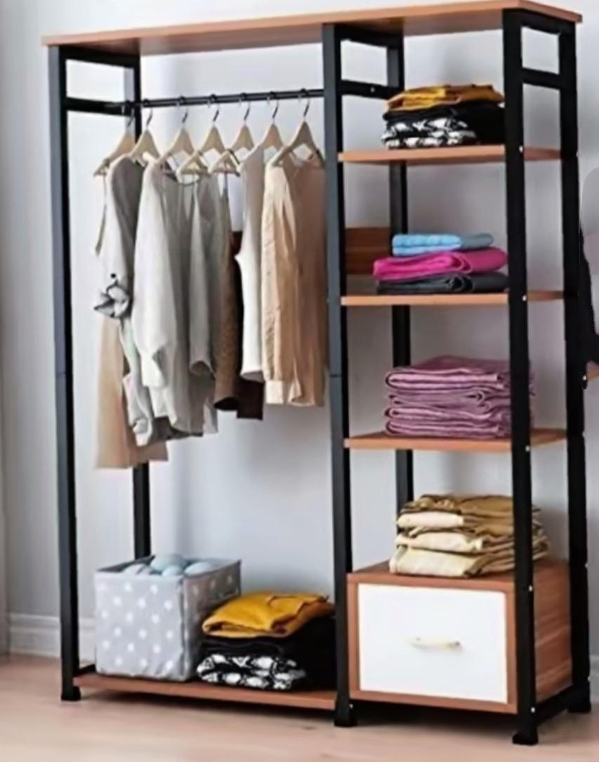 Otwarta garderoba z drewnianymi półkami i czarną metalową ramą, ubrania wiszące na wieszakach, złożone tekstylia na półkach i w koszu na dole.